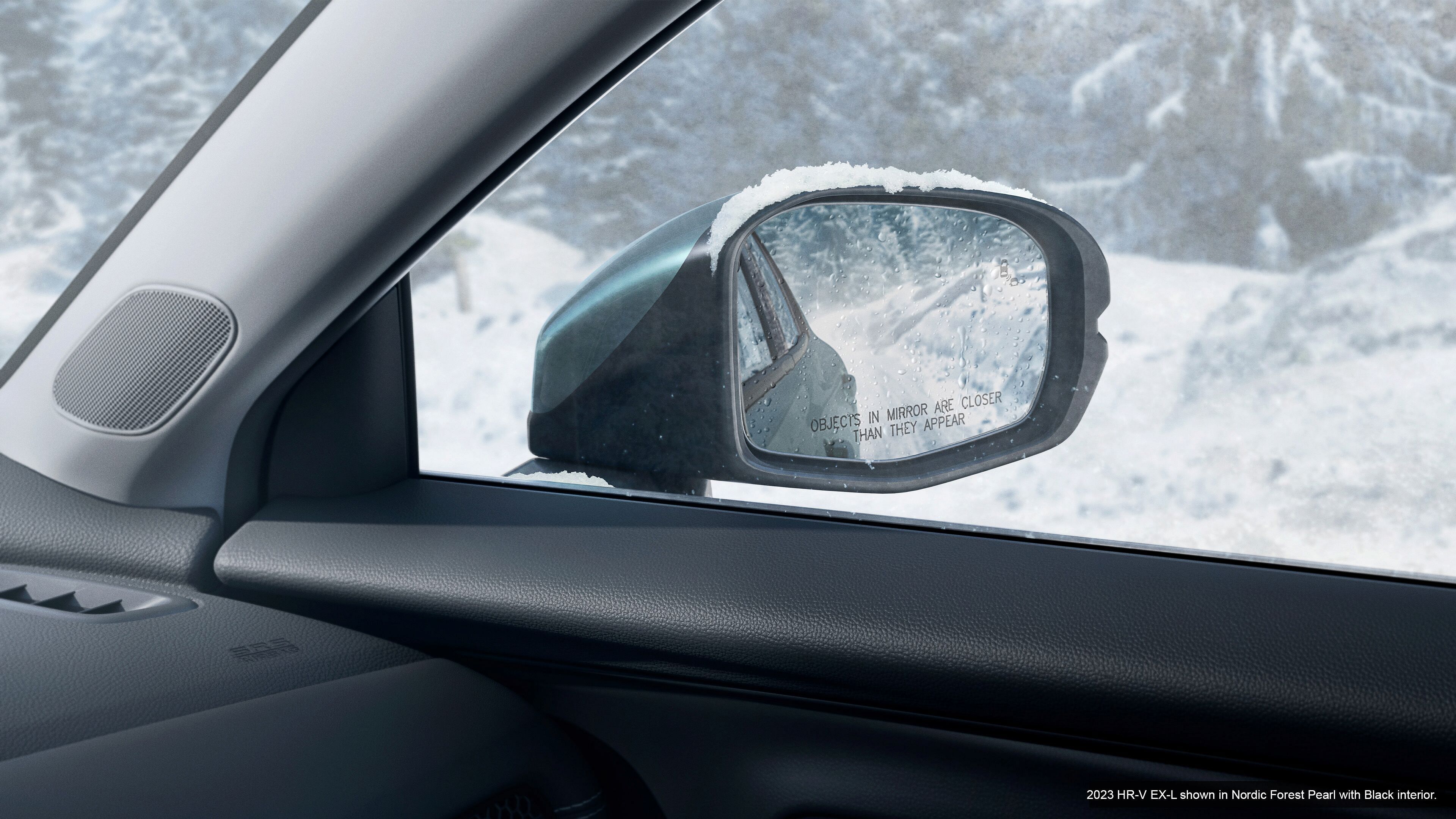 Left mirror in Honda HR-V EX-L 2023 Nordic Forest Pearl with black interior. Winter forest in the background